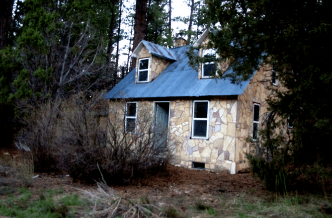 A small stone house surrounded by trees and overgrown vegetation.